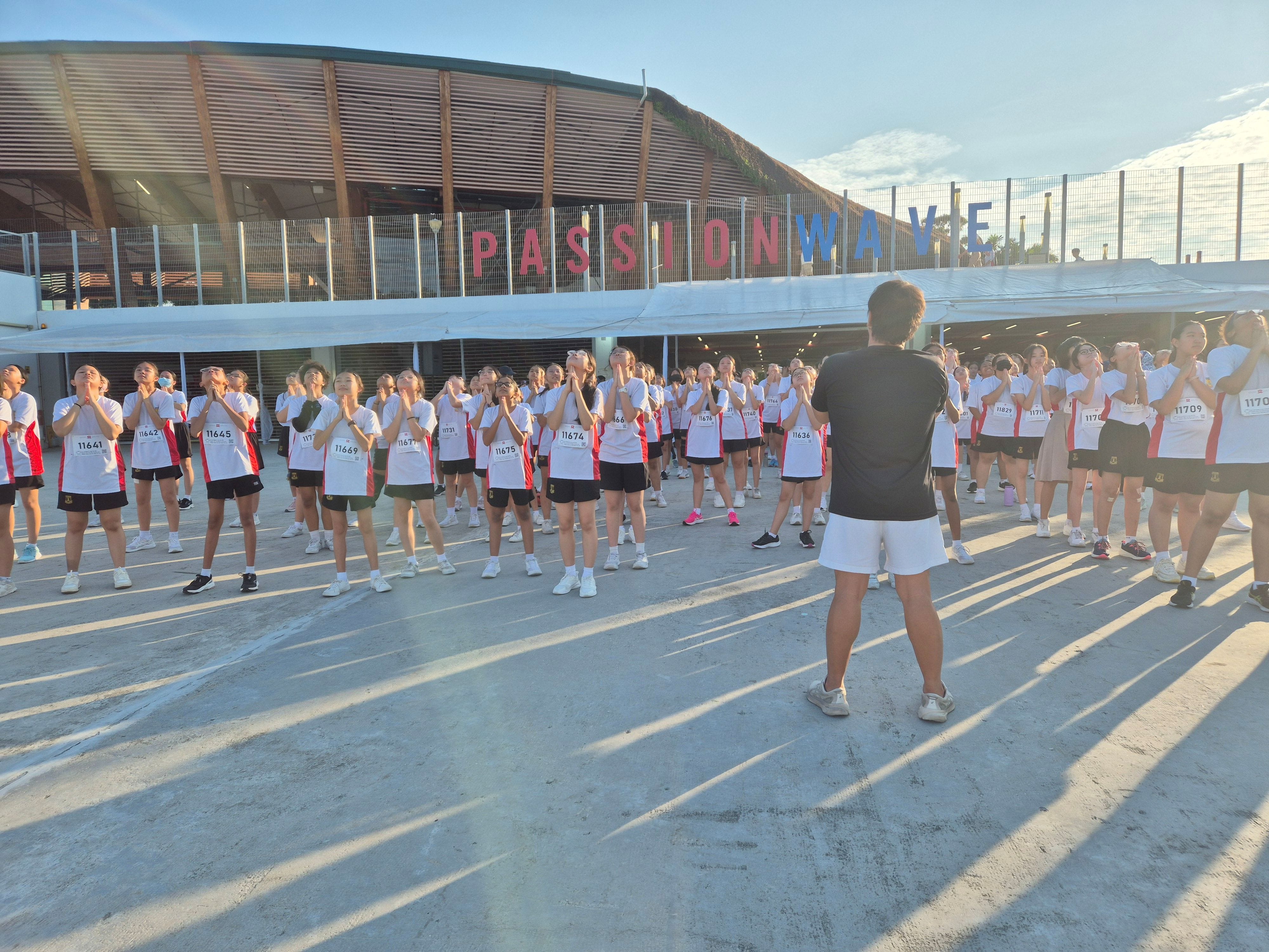 A large group of BDS students perform warm-up stretches together outdoors at the PAssion Wave facility during an outdoor education event.
